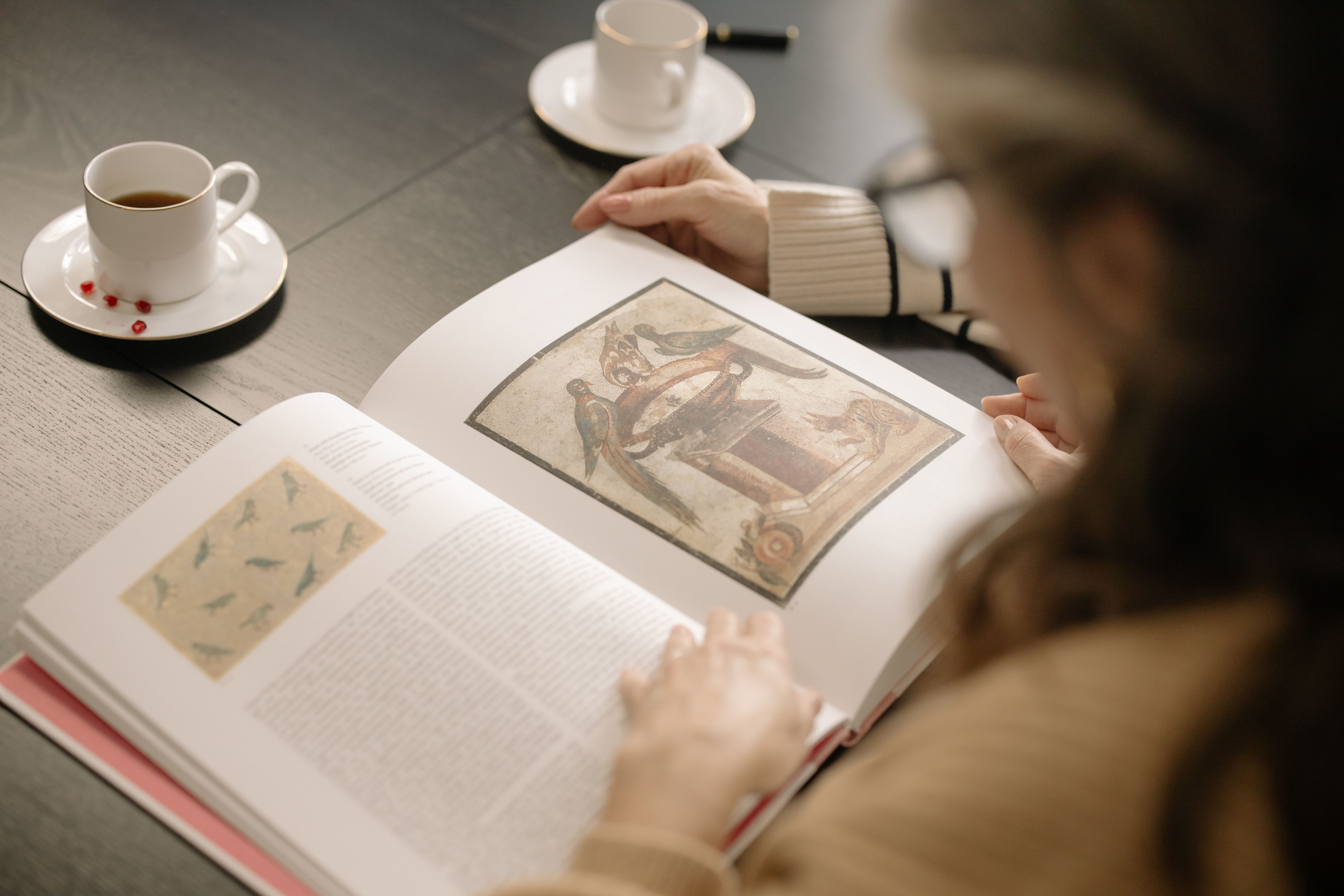 A cozy scene of a person reading an art book with coffee cups on a table.