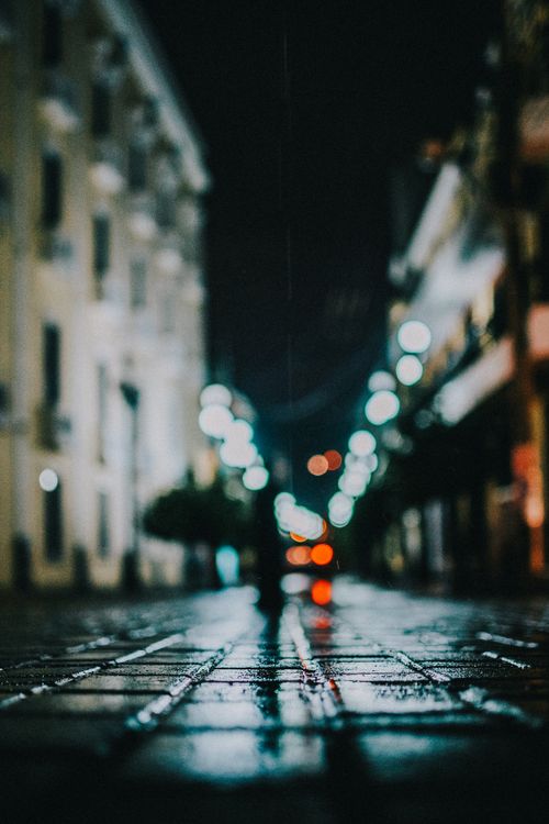 Free A dark, atmospheric street scene at night with wet pavements and blurred city lights. Stock Photo