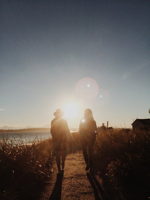 Silhouette of Two People Walking Near Body of Water during Golden Hour