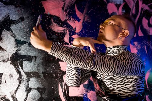Free Man in zebra pattern outfit taking a selfie against a colorful artistic background. Fashionable and stylish. Stock Photo