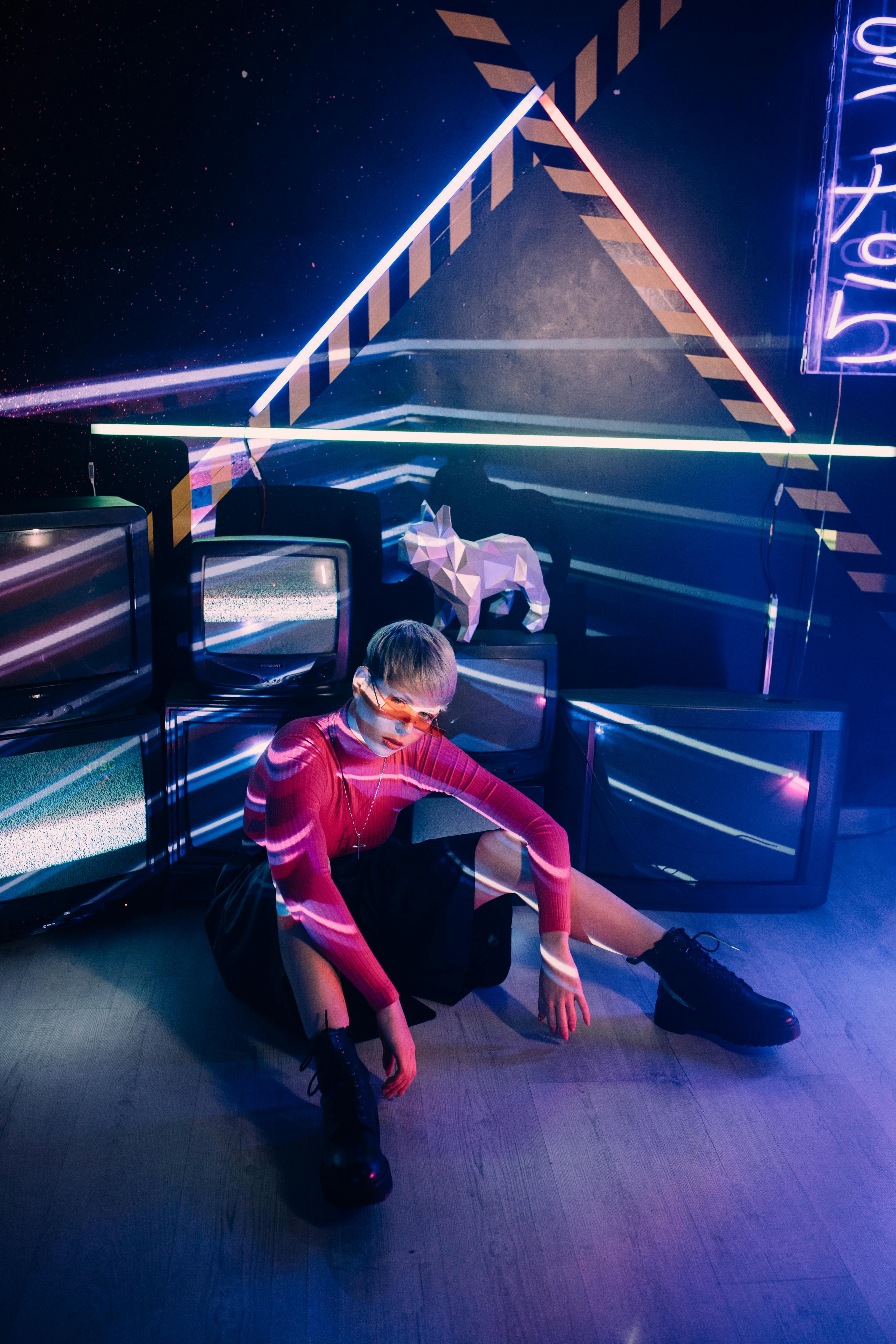 A person in vibrant neon lighting with a geometric and retro-futuristic backdrop.