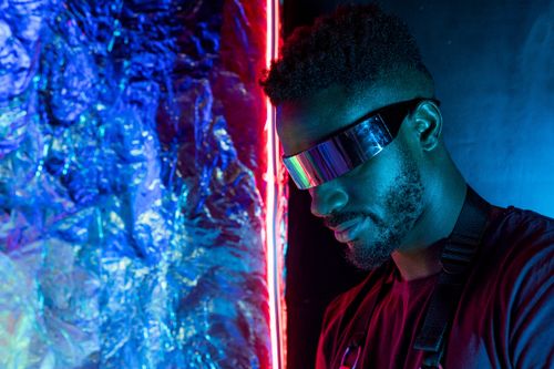 Free Portrait of a man wearing futuristic sunglasses illuminated by vibrant neon lighting, creating a modern and abstract atmosphere. Stock Photo