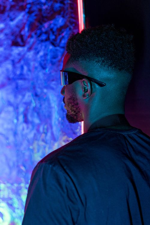 Free A man in sunglasses and black T-shirt under neon lights creating a cyberpunk techno vibe. Stock Photo