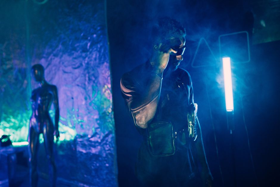 Man in leather jacket adjusting eyewear in cyberpunk setting with neon lights and smoke.