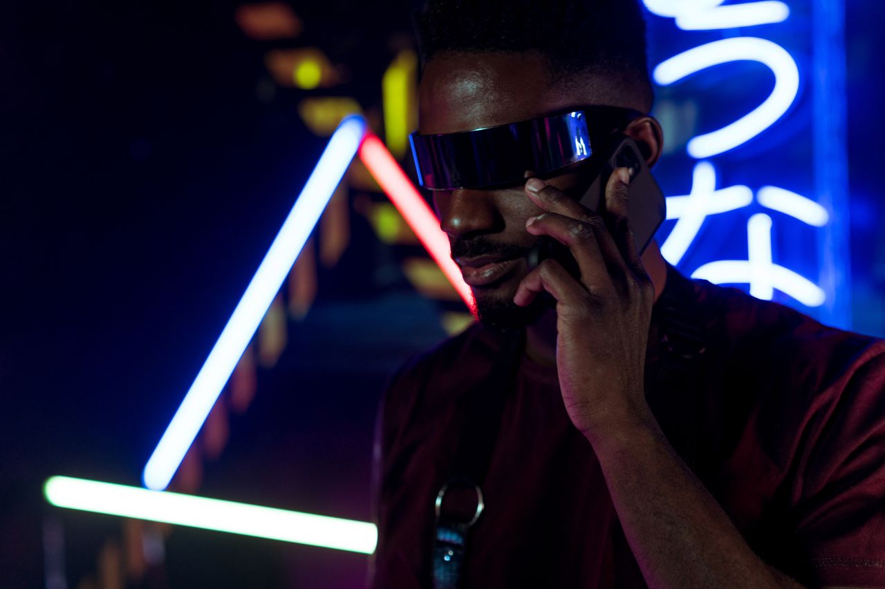a man in futuristic sunglasses talks on a smartphone surrounded by neo