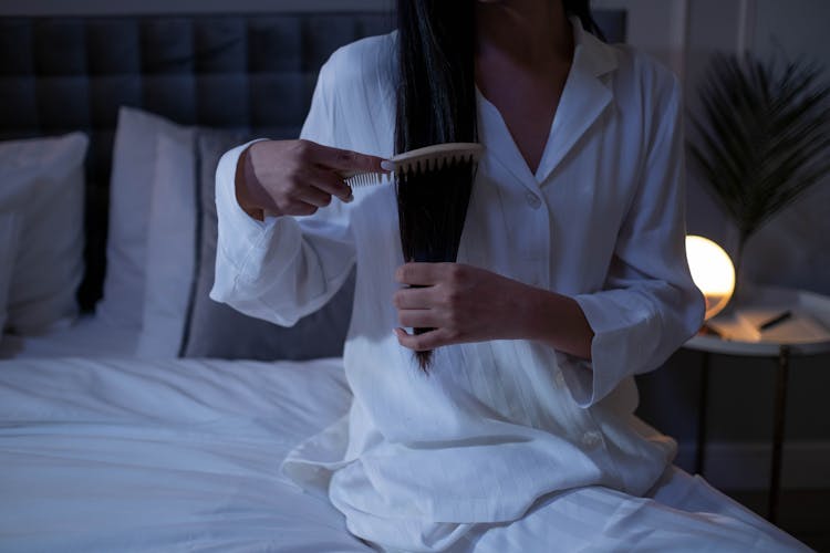 Person Sitting On The Bed While Brushing Her Hair