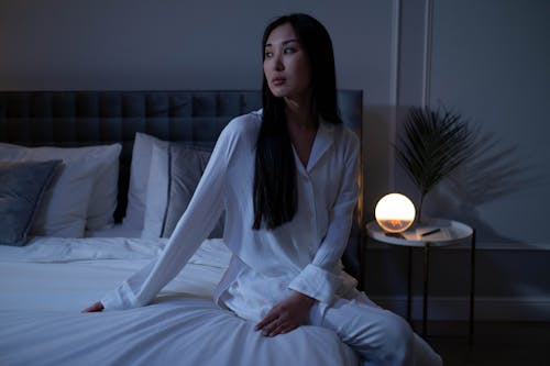 Free A Pretty Woman in White Sleepwear Sitting on a Bed Stock Photo