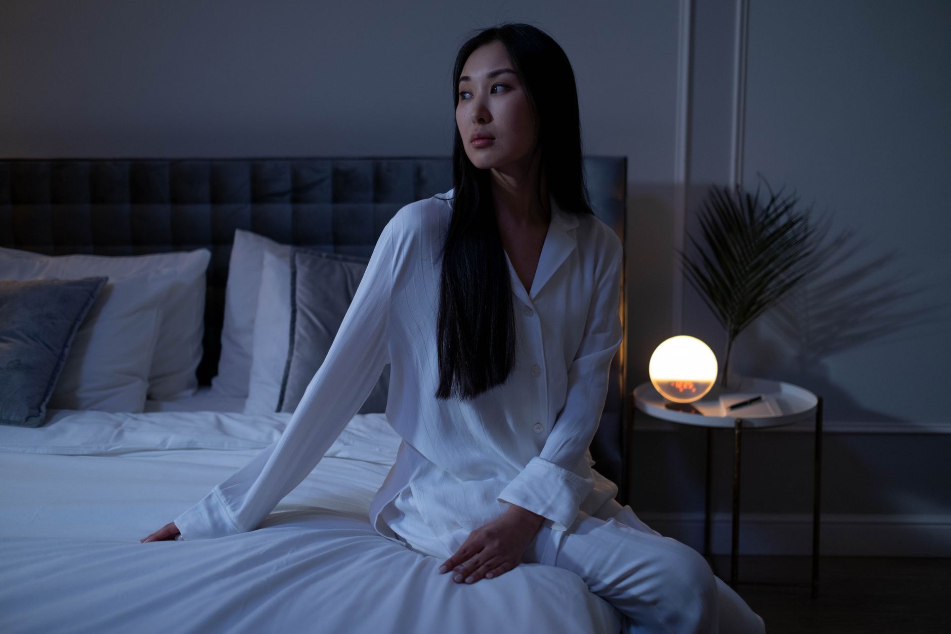 Woman in white pajamas sitting on a bed with warm lighting, showcasing a calm evening indoors.
