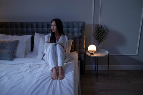 Woman in White Pajamas Sitting on Bed