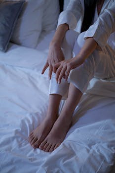 A person in pajamas sits barefoot on a bed, creating a serene and calm atmosphere.