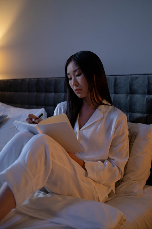 Free Woman Wearing White Sleepwear Sitting on Bed Stock Photo
