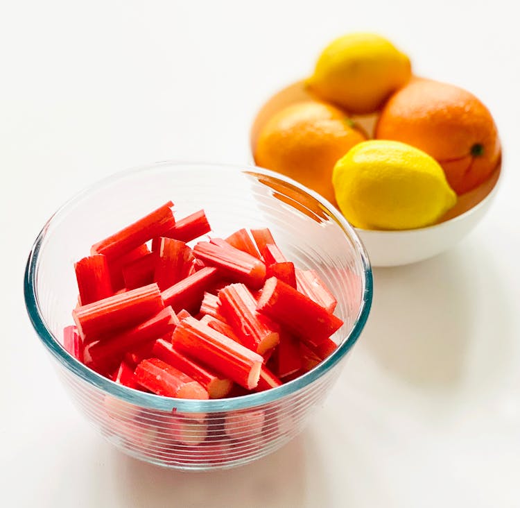 Close-Up Shot Of Sliced Rhubarb In A Clear Bowl Near Oranges And Lemons