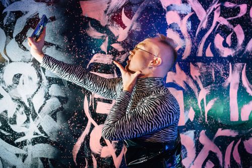 Free Man posing with smartphone in front of colorful graffiti wall. Stock Photo