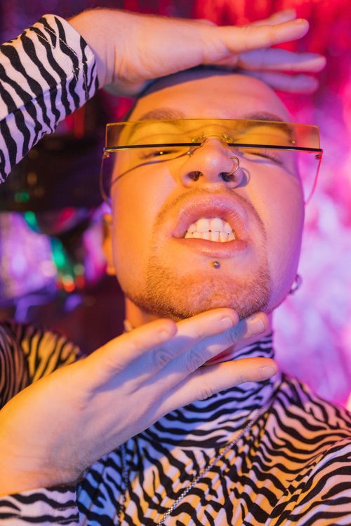 Free Close-up of an edgy man with sunglasses and piercings in vibrant neon lighting, showcasing cyberpunk aesthetics. Stock Photo
