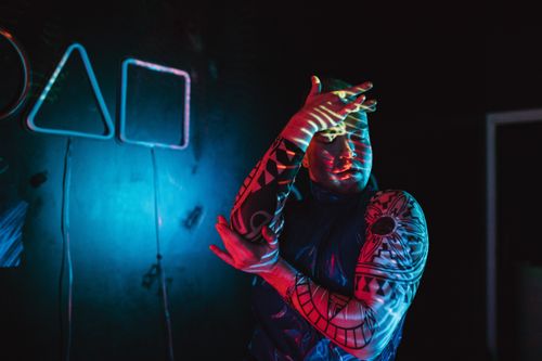 Free A man showcasing tattoos poses creatively under neon lights. Stock Photo