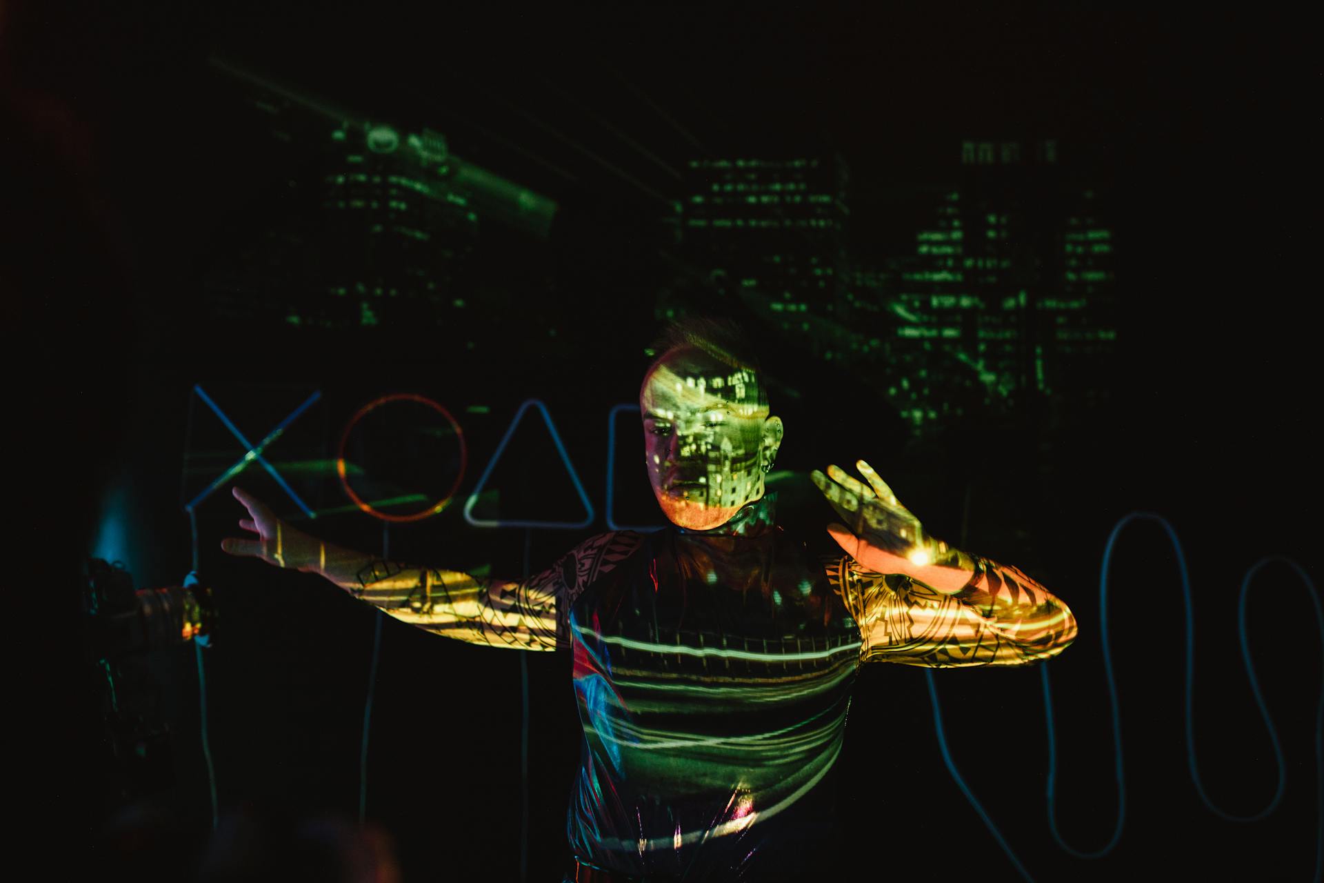 A man stands in darkness with vibrant futuristic cityscape projections covering him.