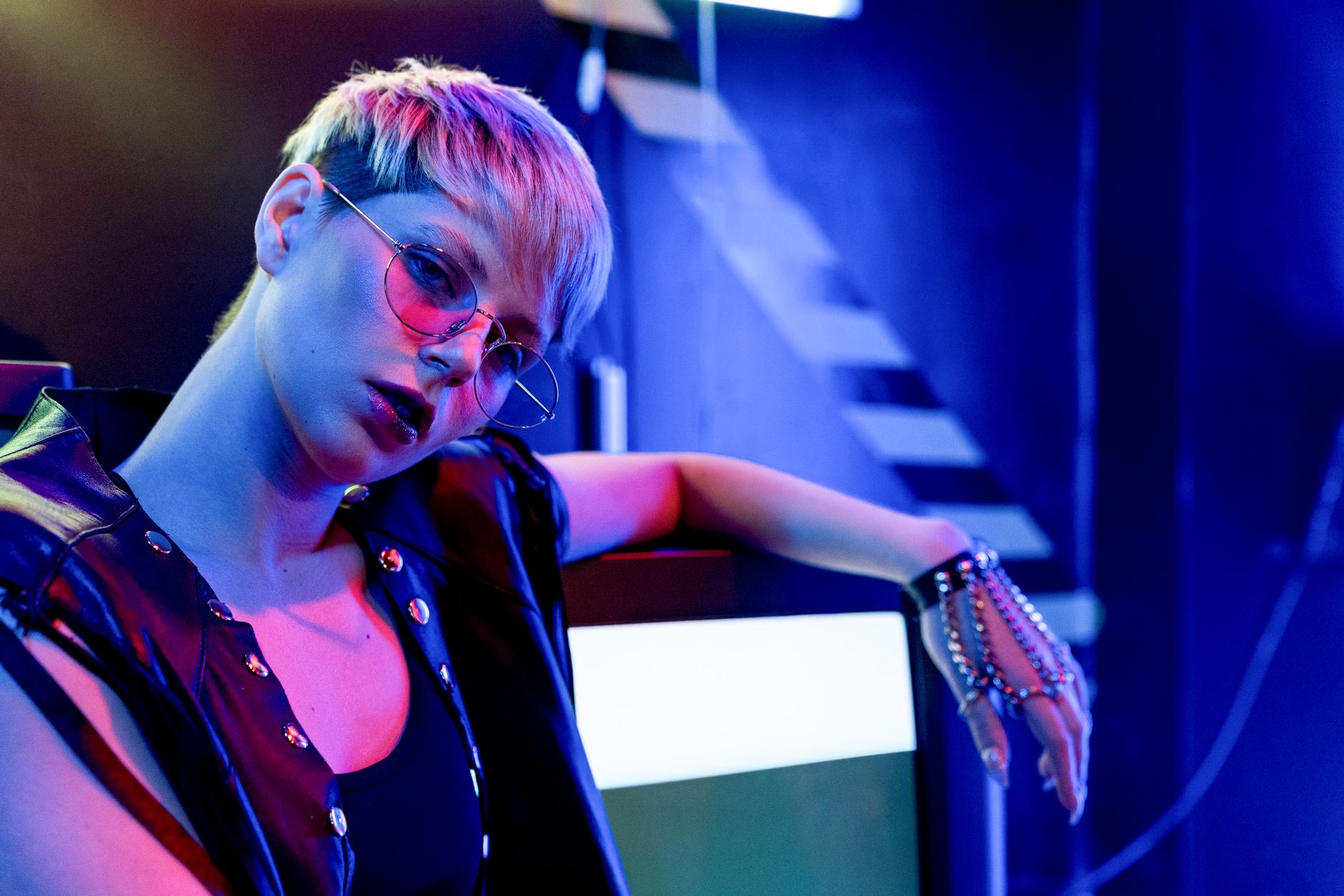 How to Choose Eyeglasses That Reflect Your Personality and Style 2 Fashionable woman in a black tank top and leather vest under vibrant neon lights with eyewear.