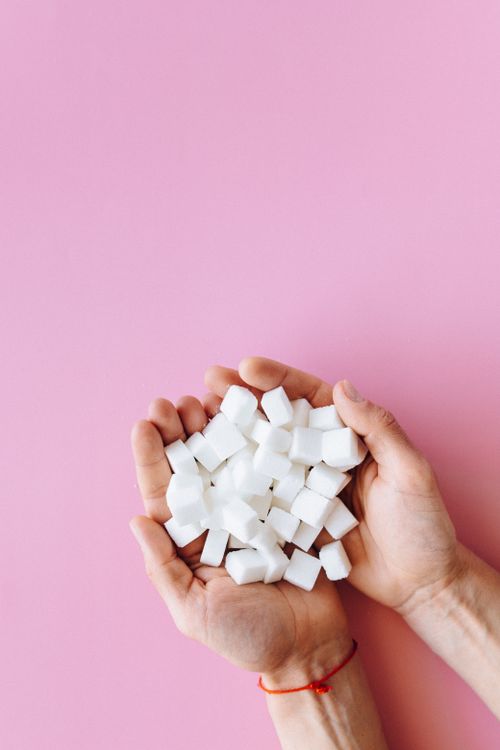 Free Open hands holding sugar cubes against a vibrant pink surface, symbolizing sweetness and health awareness. Stock Photo