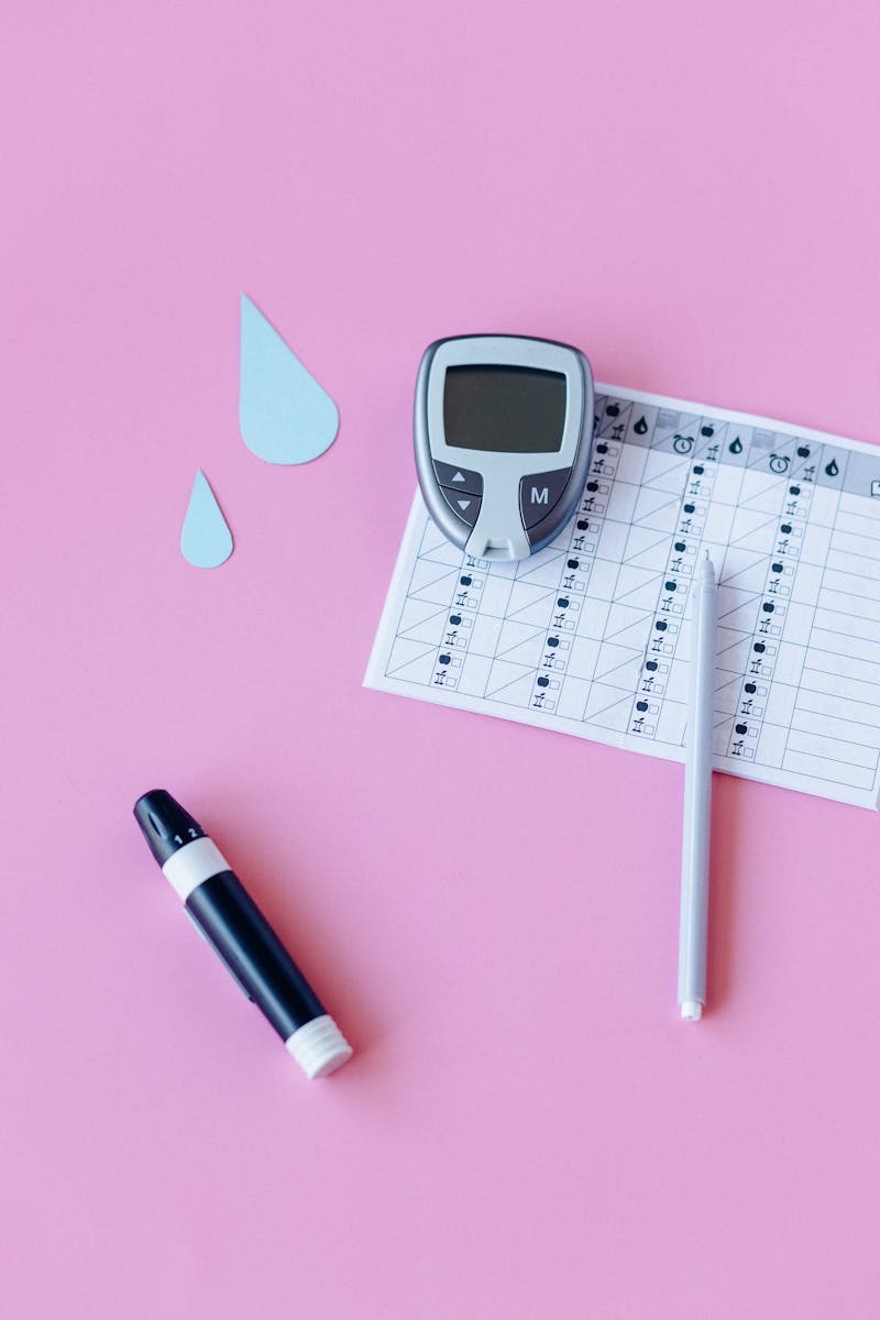 Flat lay of diabetes monitoring tools on a pink background.