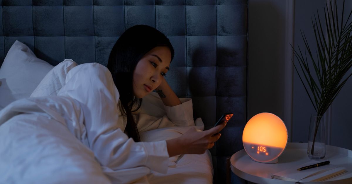 A woman in bed beside a glowing sunrise alarm clock