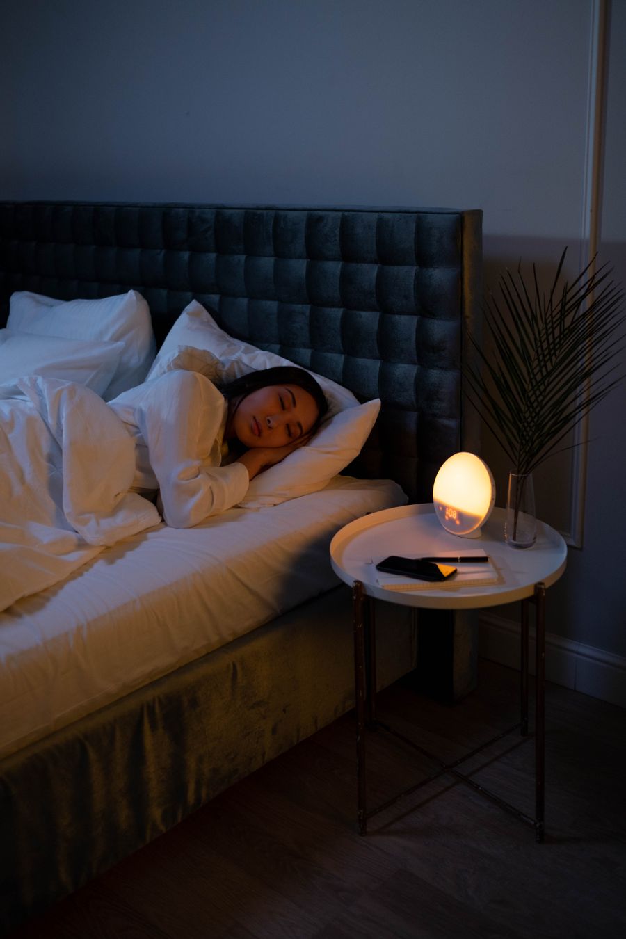 A woman sleeping calmly in a dim bedroom with a warm bedside lamp glowing softly.