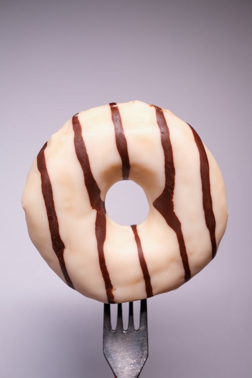 Appetizing traditional donut with white and chocolate glaze on fork against gray background