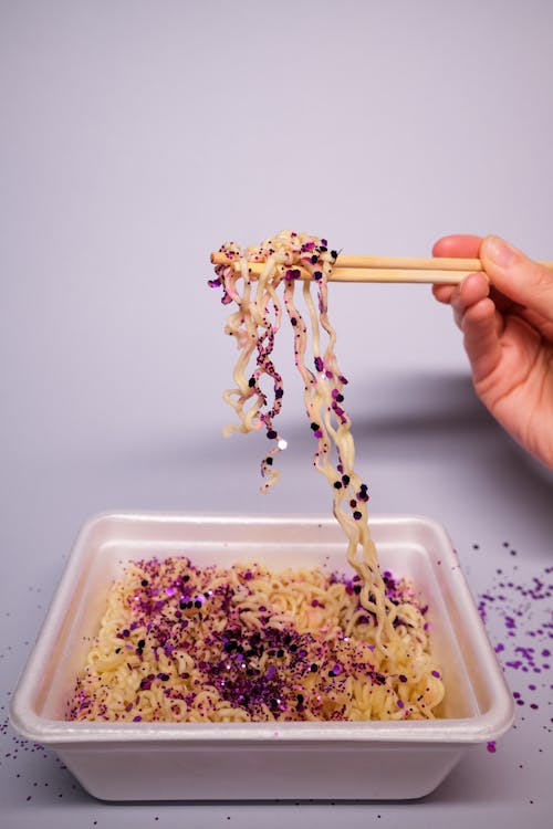 Crop unrecognizable person eating instant noodles with Asian chopsticks in plastic container placed on table