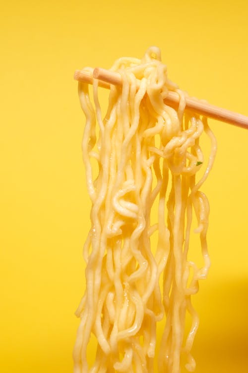 Traditional wooden Asian chopsticks with simple instant noodles against bright yellow background in studio
