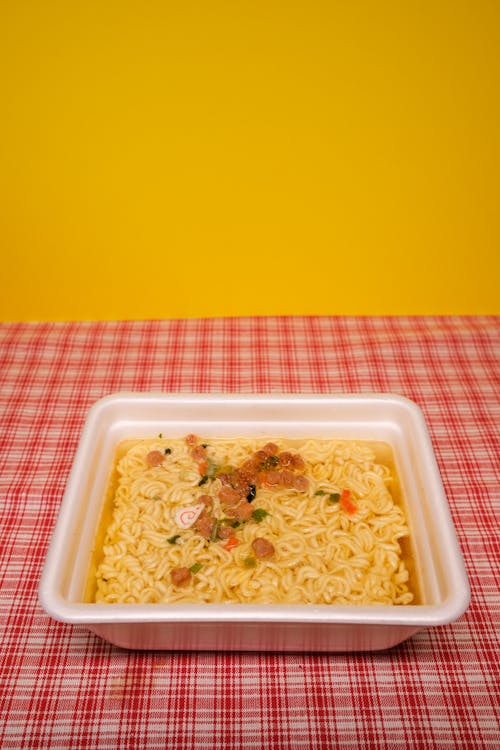 From above of plastic container with dried instant noodles with chopped veggies served on table in kitchen