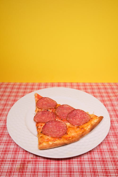 From above of slice of appetizing homemade pizza with sausages paced on plate served on table in kitchen