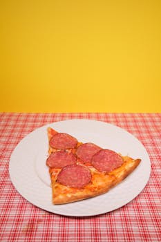 From above of slice of appetizing homemade pizza with sausages paced on plate served on table in kitchen