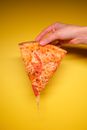 Unrecognizable person with slice of pizza on yellow background