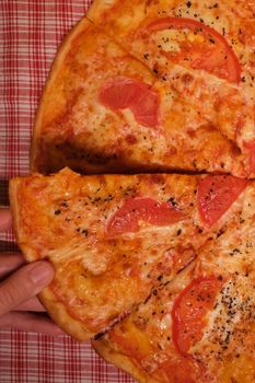 Top view of crop unrecognizable male near table with pizza slices with tomatoes and cheese with seasoning