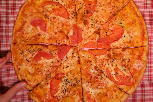 Top view of crop faceless person at table with pizza slices with tomatoes and cheese with seasoning