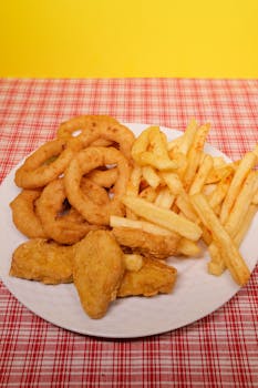 High angle of fried potato with onion rings and nuggets on plate on table near yellow wall