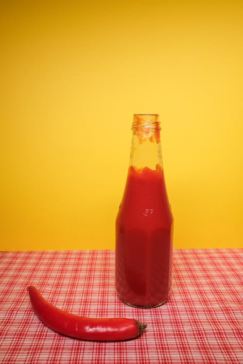 Free Bottle with ketchup near red chili pepper on table Stock Photo