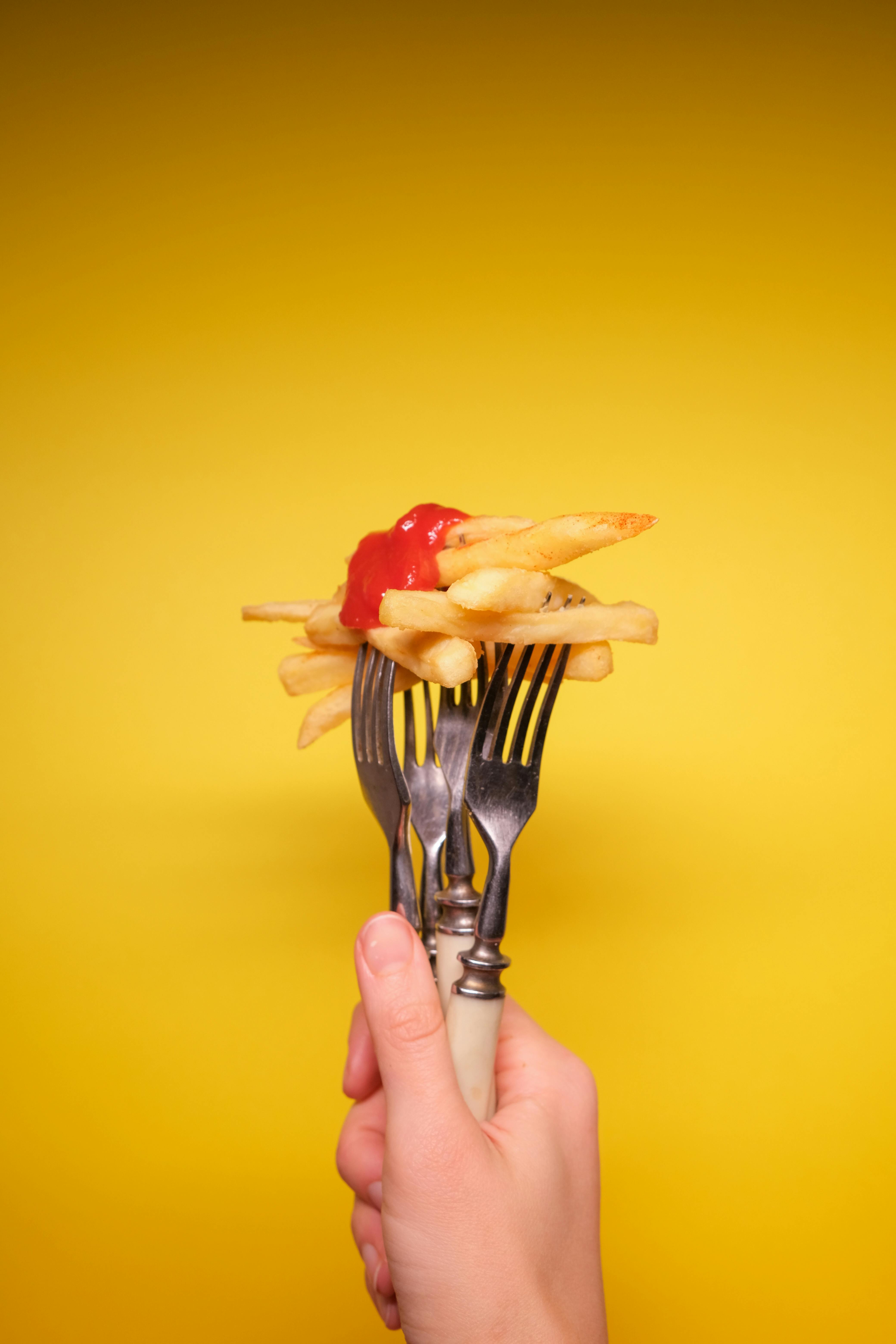 unrecognizable person with forks with french fries with ketchup