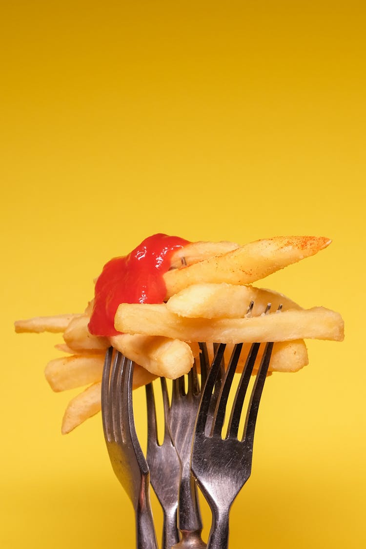 Forks With Fried Potatoes With Ketchup On Yellow Background