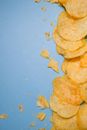 Top view of tasty golden potato chips on blue surface in light studio