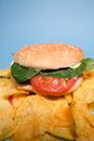 Chips near burger with tomatoes and salad on blue background