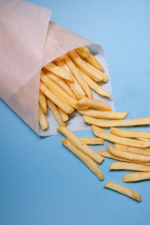 From above of fried potatoes in paper placed on blue background in bright studio