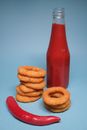 Chili pepper near ketchup and onion rings on blue background