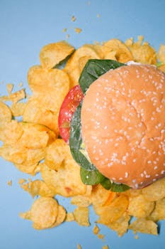 Top view of a tasty burger surrounded by crispy potato chips on a vibrant blue surface.