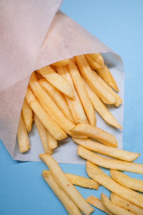 French fries wrapped in paper on blue surface