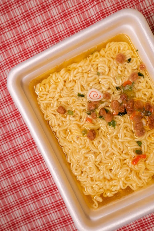 Top view of table with instant noodles in plastic box with vegetables and meat with herbs in liquid