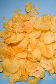 A pile of golden, crispy potato chips on a bright blue background, perfect snack imagery.