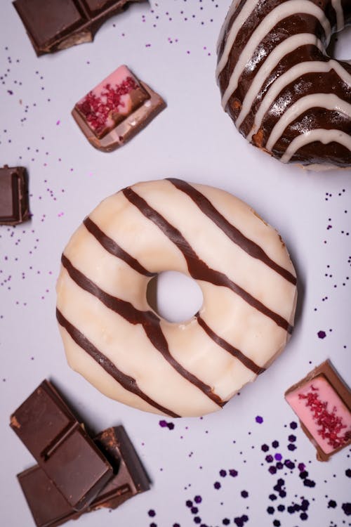 Top view of sweet glazed donuts near sweet various chocolate slices on white surface with dark spots