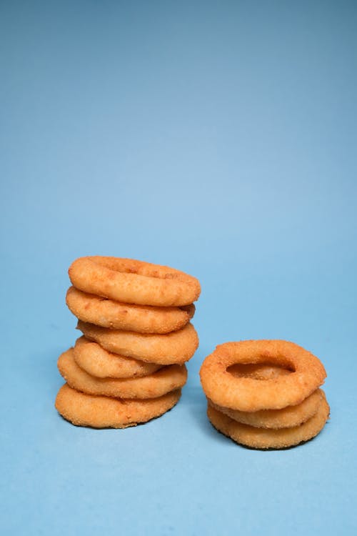 Free Golden deep fried onion rings on each other on blue background in bright studio Stock Photo