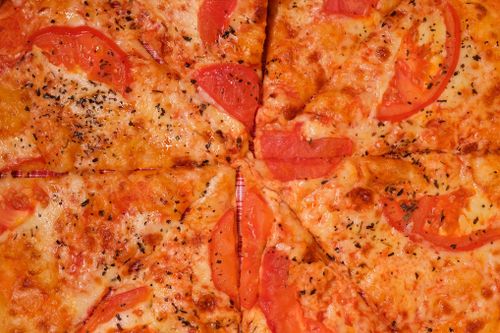 Free Full frame background of yummy pizza slices with tomatoes and cheese with seasoning placed on surface Stock Photo