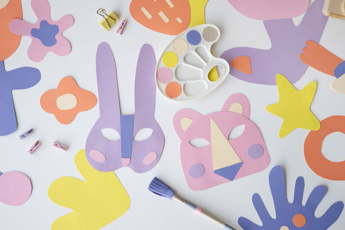 Colorful paper masks and craft materials arranged on a white table